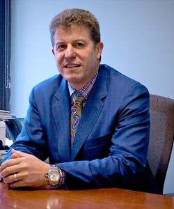 man in suit holding hand together at his desk while smirking