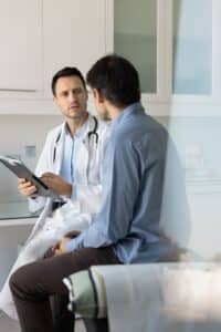Focused doctor examining a male patient in a clinic office, taking notes and discussing symptoms related to variceal bleeding and healthcare concerns in a vertical candid shot